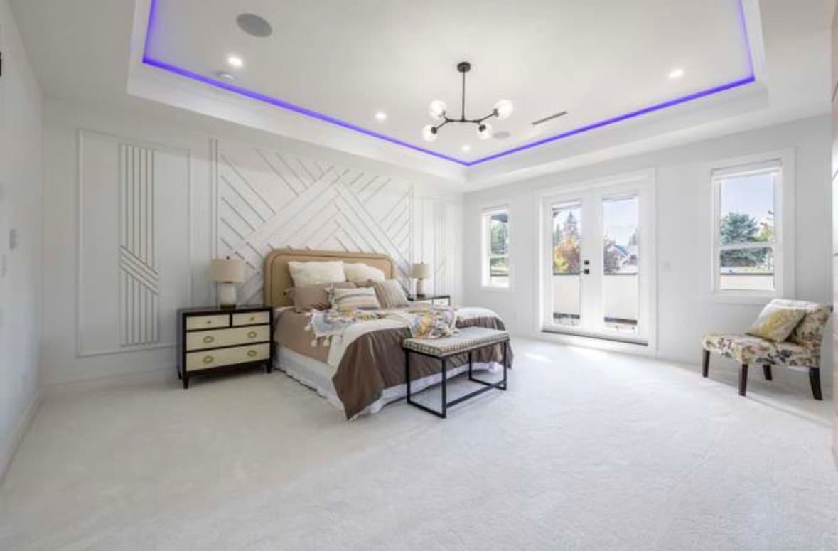 Modern bedroom with geometric wall paneling, purple LED tray ceiling, and glass balcony doors.