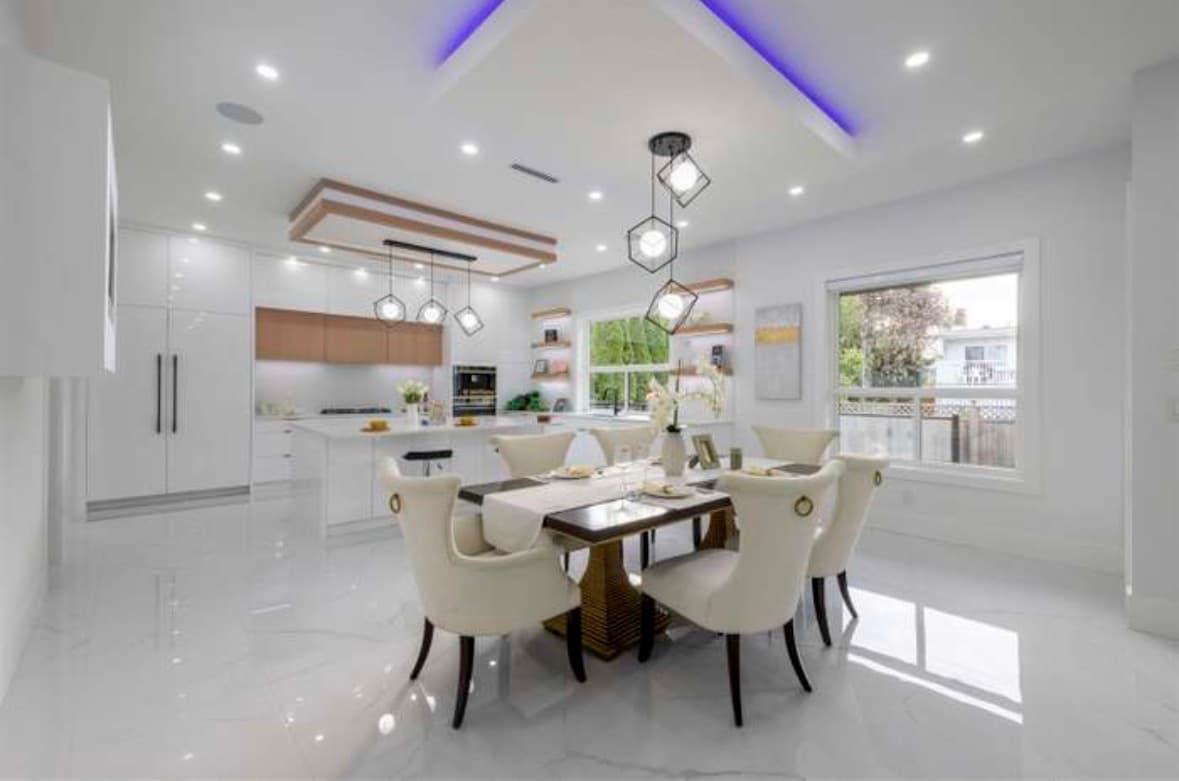 Modern open-plan kitchen and dining room with white finishes, marble floors, and stylish geometric lighting.