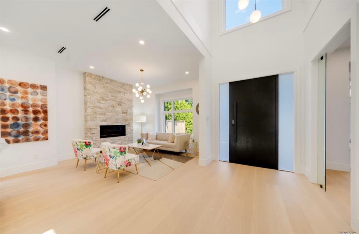 Modern living room with stone fireplace, floral armchairs, and a large black front door.