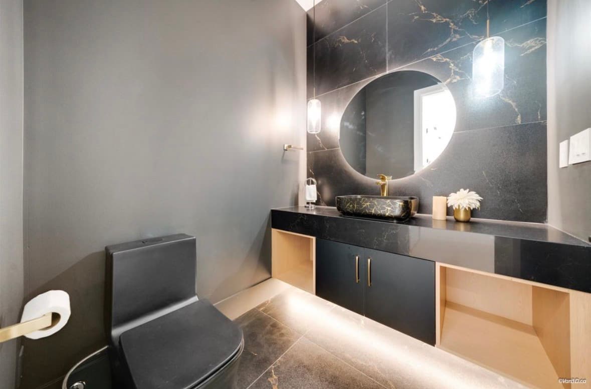 Modern dark bathroom featuring black marble walls, a round backlit mirror, and gold hardware accents.