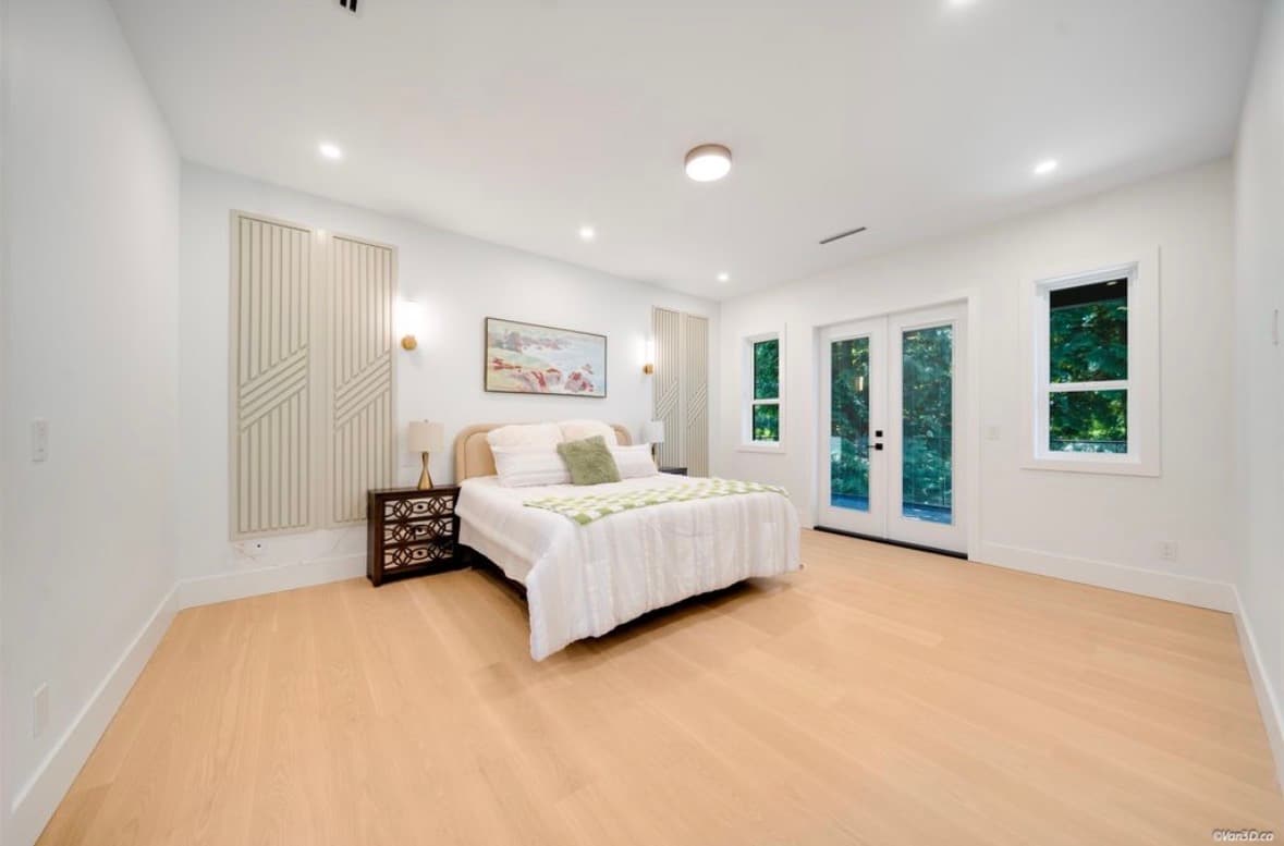 Bright modern bedroom with white bedding, light wood floors, and French doors opening to greenery.