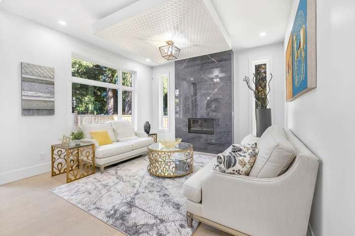 Modern living room with white sofas, gold tables, grey marble fireplace, and large windows.