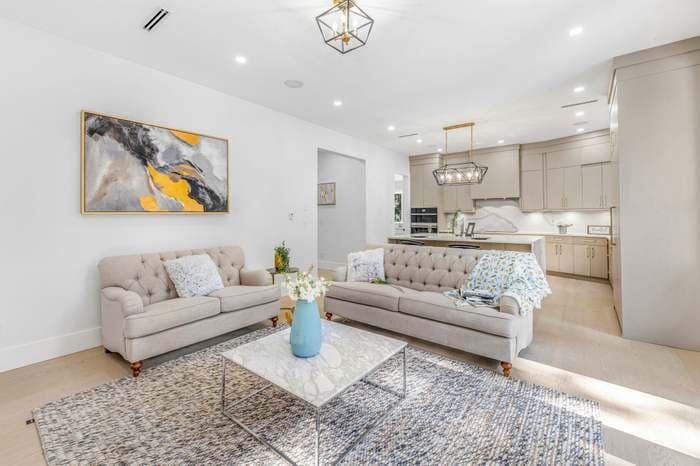 Bright living room with tufted sofas, marble table, abstract painting, and an open-concept kitchen.