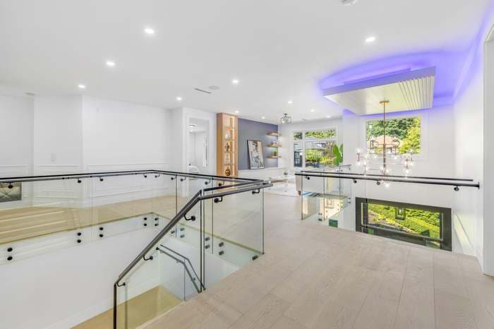 Modern interior landing with glass railings, a staircase, and a ceiling with purple LED lighting.