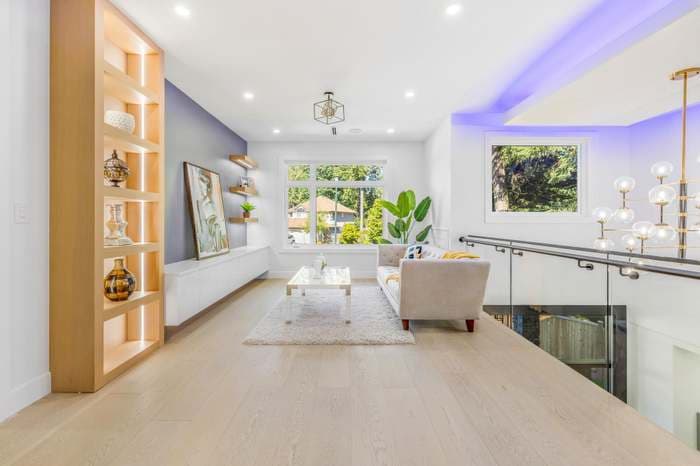 Modern living room with light wood floors, grey accent wall, and glass balcony railing.